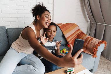 Siyahi, gülümseyen bir kadın cep telefonuyla oğlunu kucaklarken kendi fotoğrafını çekiyor.