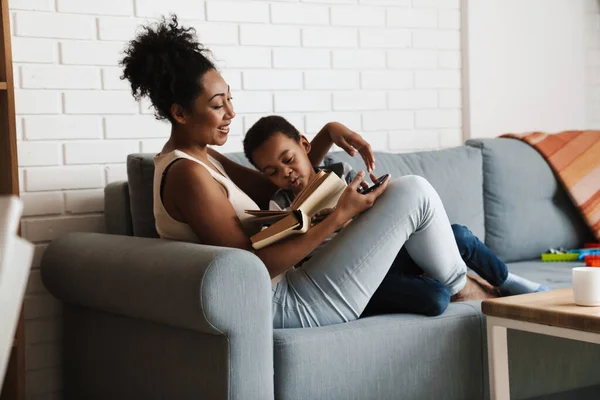 Negro Complacido Madre Hijo Leyendo Libro Mientras Está Sentado Sofá — Foto de Stock