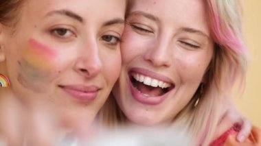 Gülümseyen bir kadının yakın çekim görüntüsü cep telefonuyla selfie çekerken birbirlerini öperek gurur yürüyüşünün tadını çıkarıyorlar.