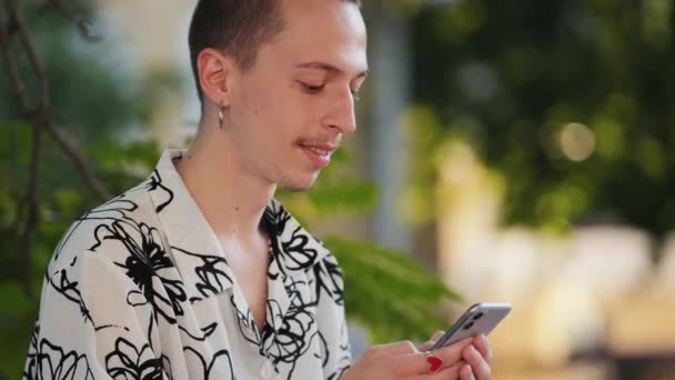 Een Lachende Hipster Met Oorbellen Gebruikt Zijn Telefoon Buiten — Stockvideo