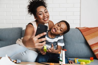 Siyahi, gülümseyen bir kadın cep telefonuyla oğlunu kucaklarken kendi fotoğrafını çekiyor.