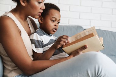 Siyah anne ve oğul evdeki kanepede otururken kitap okuyor.