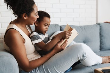 Evdeki kanepede otururken siyah anne ve oğlu kitap okuyorlar.