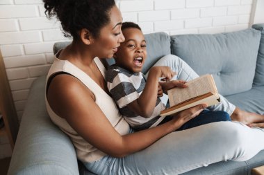 Evdeki kanepede otururken siyah anne ve oğlu kitap okuyorlar.