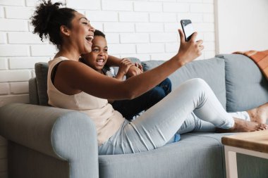 Siyahi, gülümseyen bir kadın cep telefonuyla oğlunu kucaklarken kendi fotoğrafını çekiyor.