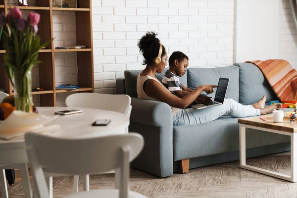 黒人の母親と息子は自宅でソファに座っている間にラップトップを使用して — ストック写真