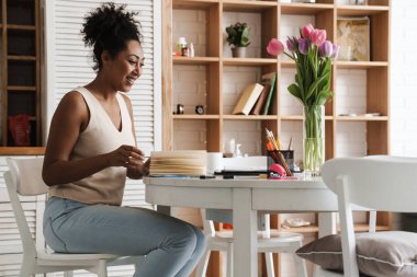Evdeki mutfaktaki masada otururken gazetelerle çalışan gülümseyen zenci kadın.