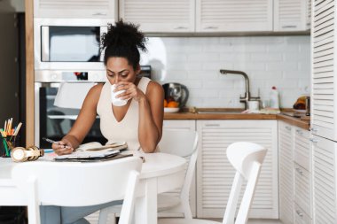 Siyah, gülümseyen kadın evde çalışırken kahve içiyor.