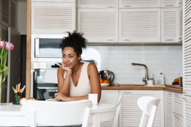 Evdeki mutfaktaki masada oturan siyahi kadın kağıtlarla çalışıyor.