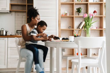 Siyahi anne ve oğul evde yan yana otururken yazıp cep telefonu kullanıyorlar.