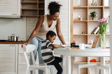 Siyah anne, oğluyla ev ödevi yaparken dizüstü bilgisayar kullanıyor.