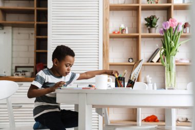 Siyah çocuk dizüstü bilgisayar kullanıyor ve evde otururken ödev yapıyor.