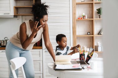Evde dizüstü bilgisayarla çalışırken cep telefonuyla konuşan siyah bir kadın.