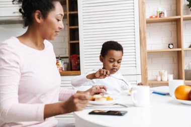 Siyah gülümseyen anne ve oğlu evde otururken birlikte kahvaltı yapıyorlar.