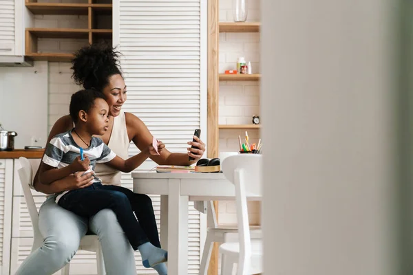 Negro Sonriente Madre Hijo Usando Teléfono Móvil Mientras Están Sentados —  Fotos de Stock