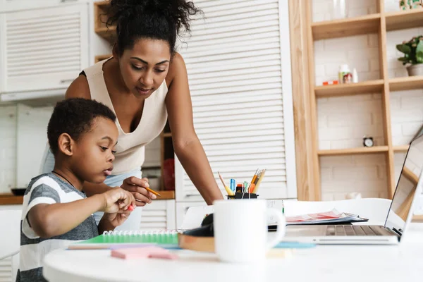 Siyah anne, oğluyla ev ödevi yaparken dizüstü bilgisayar kullanıyor.