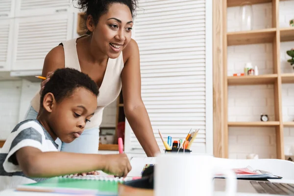Black mother using laptop while doing homework with her son at home