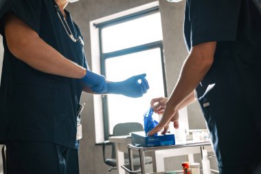 İki doktor hastalarını kabineye almaya hazırlanıyor. Eldiven takıyorlar.