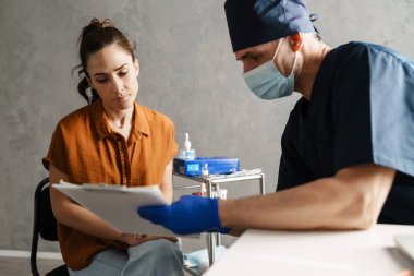 Kadın hasta ve erkek doktor muayene sırasında dolapta oturuyorlar, doktor notlar gösteriyor.