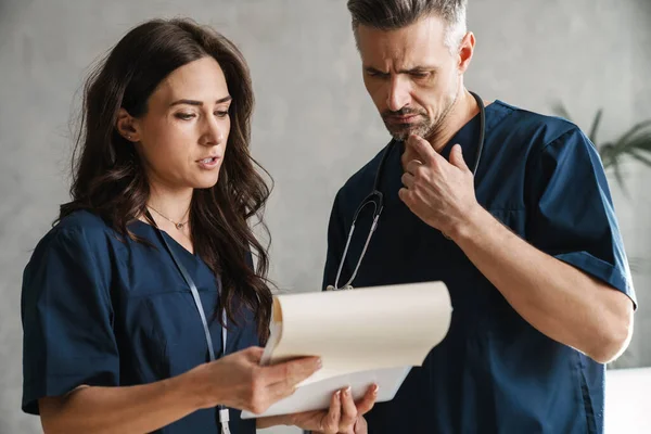 Two Serious Doctors Medical Uniform Looking Clipboard While Standing Indoors — Stock Photo, Image