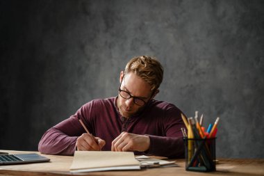 Stüdyoda bir masada otururken günlüğe bir şeyler yazan bir adam.