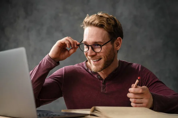 Mosolygó Férfi Belenéz Laptop Képernyőjébe Beállítja Szemüveget Miközben Stúdióban Asztalnál — Stock Fotó