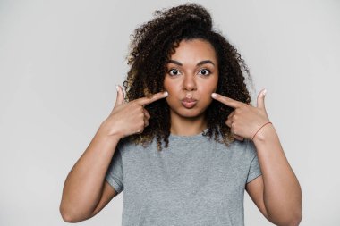 Mutlu bir kadın kameraya bakar ve ışık stüdyosunda dikilirken yanaklarına dokunur.