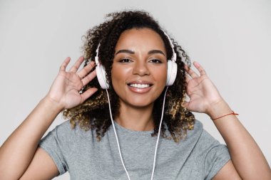 Stüdyoda dikilirken kameraya bakan kulaklıkla müzik dinleyen gülümseyen bir kadının portresi.