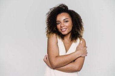 Işık stüdyosunda dururken elleri kapalı gülümseyen bir kadın.