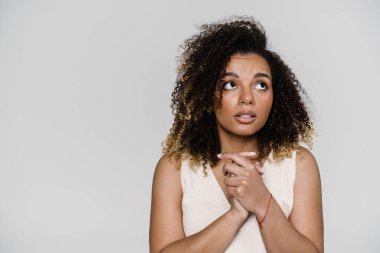 Parlak bir stüdyoda dikilirken kollarını kavuşturup yan tarafa bakan düşünceli bir kadının portresi.