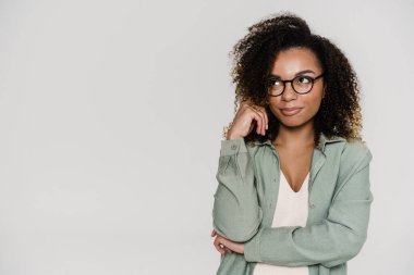 Dalgın, kıvırcık saçlı, gözlüklü bir kadın. Stüdyoda dikilirken başını yana çeviriyor.