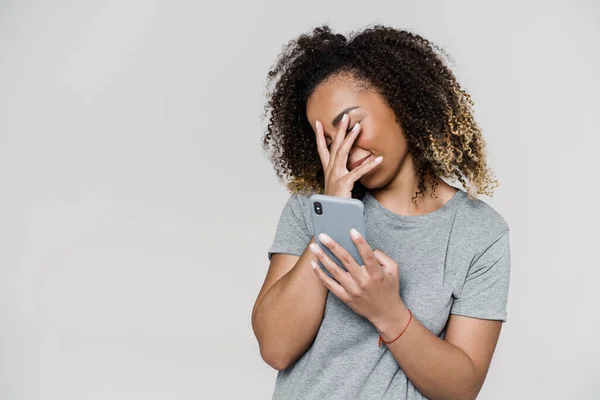 Жінка Прикриває Обличчя Рукою Тримає Телефон Стоячи Сірій Студії — стокове фото