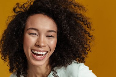 Genç Afrikalı kadın kahkaha atıyor ve kahverengi duvardan izole edilmiş kameraya bakıyor.