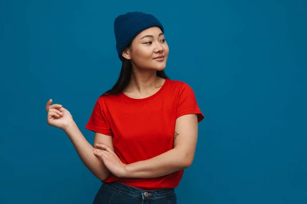 穿着休闲装的快乐的年轻亚洲女人站在蓝色的墙的背景上 把目光投向一边 — 图库照片