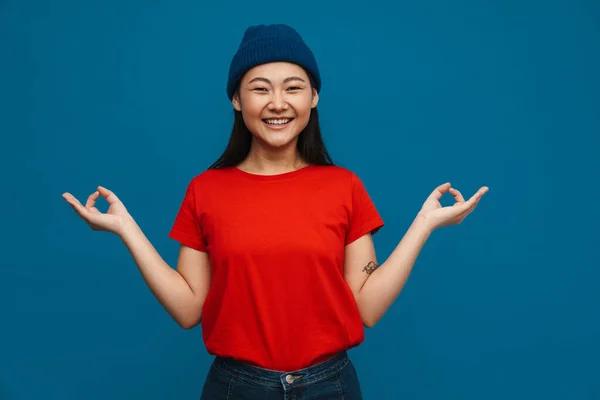 Azji Nastolatek Dziewczyna Kapelusz Uśmiech Pokazując Zen Gest Izolowane Niebieskim — Zdjęcie stockowe