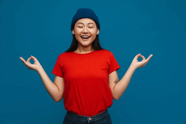 Azji Nastolatek Dziewczyna Kapelusz Uśmiech Pokazując Zen Gest Izolowane Niebieskim — Zdjęcie stockowe