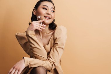 Kirpik bigudiyle poz verirken gülümseyen genç Asyalı kadın bej arka planda izole edilmiş.