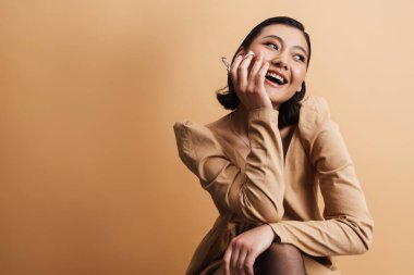 Kirpik bigudiyle poz verirken gülümseyen genç Asyalı kadın bej arka planda izole edilmiş.