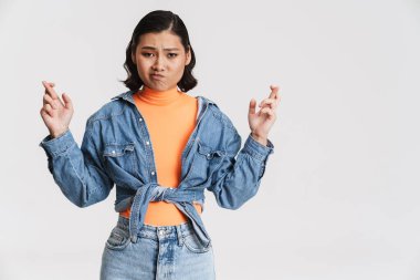 Asyalı genç bir kadın, şans dilemek için şans dilerken yüzünü buruşturuyor. Beyaz arka plan üzerinden izole edilmiş.