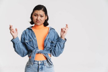 Asyalı genç bir kadın, şans dilemek için şans dilerken yüzünü buruşturuyor. Beyaz arka plan üzerinden izole edilmiş.