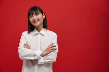 Genç Asyalı esmer kadın gülümsüyor ve kırmızı arka planda izole edilmiş kameraya bakıyor.