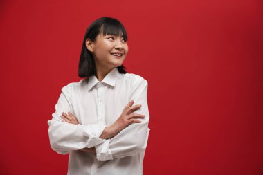 Genç Asyalı esmer kadın gülümsüyor ve kırmızı arka planda soyutlanmış bir şekilde yan tarafa bakıyor.