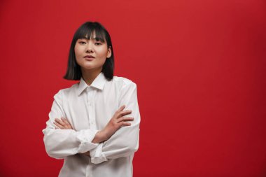 Genç Asyalı esmer kadın kırmızı arka planda yalnız poz veriyor ve kameraya bakıyor.