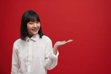 Genç Asyalı esmer kadın gülümsüyor ve kırmızı arka planda gizli bir telif alanı tutuyor.