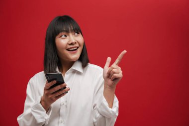 Kırmızı arka planda izole edilmiş cep telefonu kullanan Asyalı genç bir kadın.