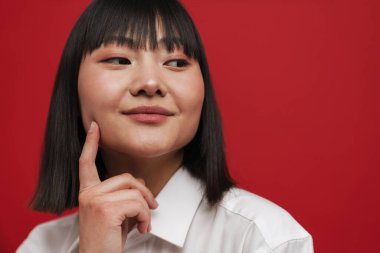 Genç Asyalı kadın yanağını işaret ediyor ve kırmızı arka planda tek başına bir kenara bakıyor.