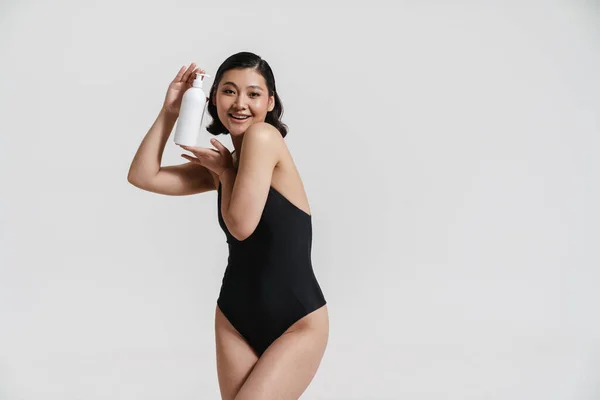 水着を身に着けているブルネットアジアの女性は笑顔と白い背景に隔離された美しさの製品を示す — ストック写真