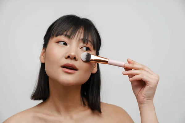 Mulher Sem Camisa Asiática Usando Escova Enquanto Faz Maquiagem Isolada — Fotografia de Stock