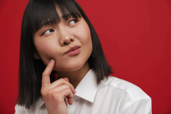 年轻的亚洲女人用手指指指着她的脸颊 在红色的背景下孤立地望着旁边 — 图库照片