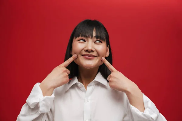 年轻的亚洲女人微笑着 用手指指指着被红色背景隔开的脸颊 — 图库照片